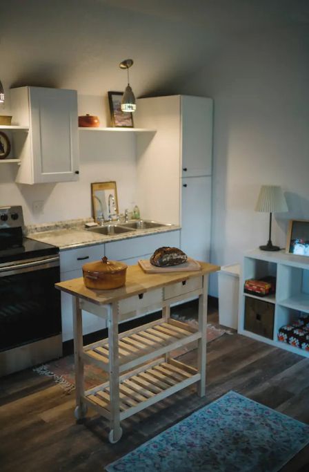 Een gezellige keuken met witte kastjes, een houten aanrecht, een hanglamp en een tafeltje met een mand.