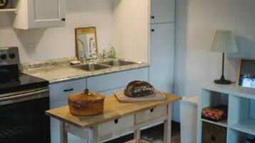 Een gezellige keuken met witte kastjes, een houten aanrecht, een hanglamp en een tafeltje met een mand.