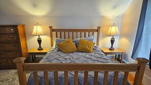 A bed with a wooden frame, two bedside tables with lamps, a wooden dresser, and a patterned rug. - Flinthills Premier Getaway (Severy)