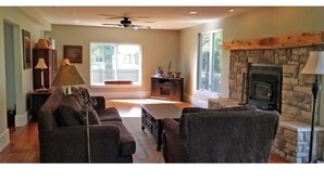 A living room with a stone fireplace, a ceiling fan, and a view of a deck. - Flinthills Premier Getaway (Severy)