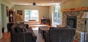 A living room with a stone fireplace, a ceiling fan, and a view of a deck. - Flinthills Premier Getaway (Severy)