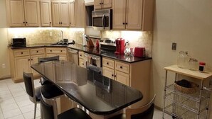 A kitchen with beige cabinets, a black countertop, a stainless steel microwave, a red coffee maker, and a metal cart with a basket. - EAT, DRINK, PLAY & RELAX in Windham (Windham)