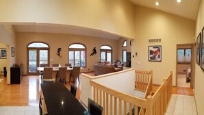 A spacious living area with a long dining table, a wooden railing, and large windows. - EAT, DRINK, PLAY & RELAX in Windham (Windham)