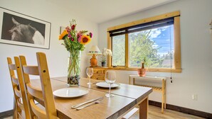 A dining area with a wooden table, chairs, a vase with flowers, a lamp, and a window with a view of trees. - Lovely Spacious Home In Downtown White Salmon (White Salmon)