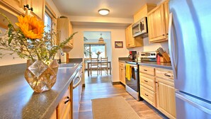 A modern kitchen with wooden cabinets, a stainless steel refrigerator, and a dining area with a table and chairs. - Lovely Spacious Home In Downtown White Salmon (White Salmon)
