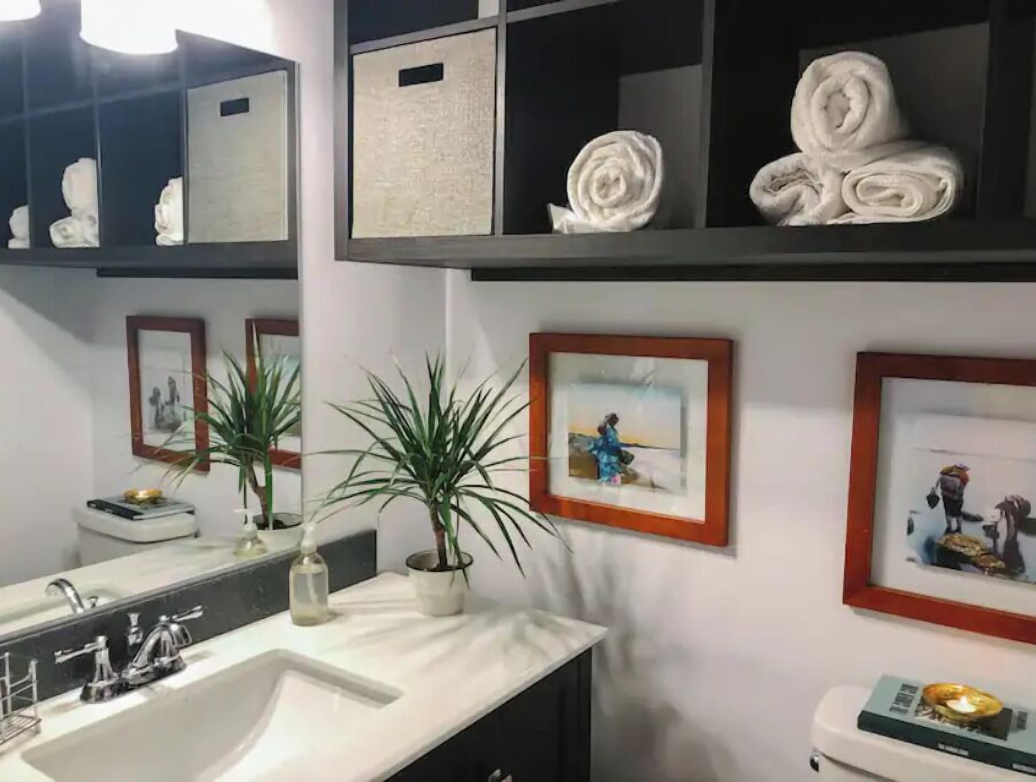 Ein Badezimmer mit einem weißen Waschbecken, zwei topfgepflanzten Pflanzen und gerahmten Bildern an der Wand.