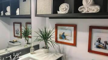 Ein Badezimmer mit einem weißen Waschbecken, zwei topfgepflanzten Pflanzen und gerahmten Bildern an der Wand.
