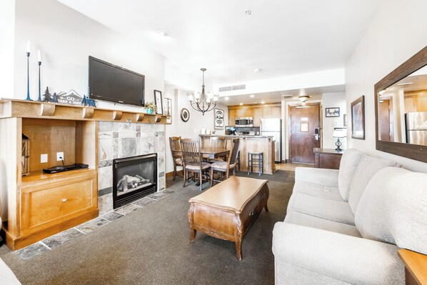 A spacious living room with a fireplace, a television, and a dining area with chairs and a table. - Sundial B216 | Ski-in/Ski-out | Mountain Views | Pools & Hot Tubs | Great Amenities (Park City)