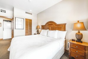 A hotel room with a large bed, wooden headboard, bedside lamp, and a nightstand with a clock. - Sundial B216 | Ski-in/Ski-out | Mountain Views | Pools & Hot Tubs | Great Amenities (Park City)