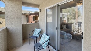 Un balcon avec deux chaises, une porte vitrée et une vue sur un immeuble voisin.