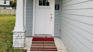 A house with a white front door, a small window above the door, and a red and beige striped mat at the entrance. - Brand New Construction 🏠 Resort style Getaway (Jacksonville)
