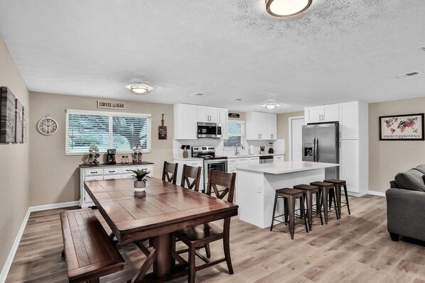 A modern kitchen with white cabinets, a dining area with a wooden table and benches, and a bar area.