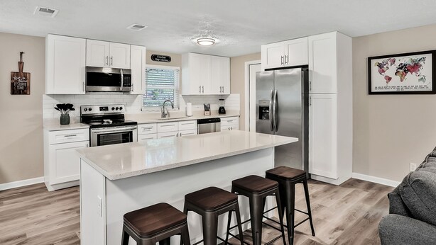 A modern kitchen with white cabinets, stainless steel appliances, and a central island with stools. - ⭐️Stylish 3/2 🏡 fully renovated in Orange Park⭐️ (Orange Park)