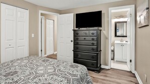 A bedroom with a bed, a dresser, a television, and a bathroom visible through an open door. - ⭐️Stylish 3/2 🏡 fully renovated in Orange Park⭐️ (Orange Park)