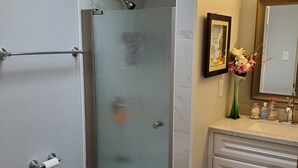 A bathroom with a glass shower enclosure, a toilet, and a vanity with a mirror.