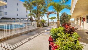 A pool area with a white fence, palm trees, and a building with balconies.