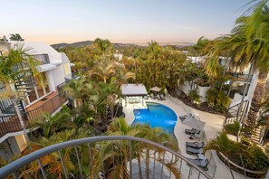 Zona de piscina en la azotea con vistas a la ciudad, rodeada de palmeras y edificios modernos.