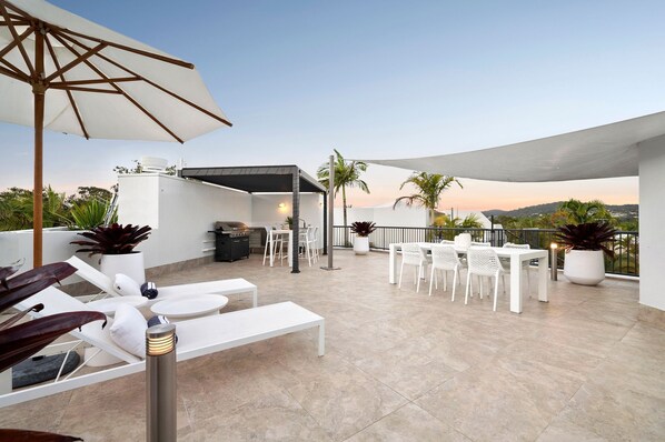 Una terraza en la azotea con sillones blancos, una mesa de comedor y plantas en macetas.