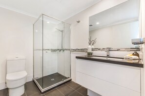 Un baño moderno con ducha de vidrio, inodoro blanco y tocador con espejo.