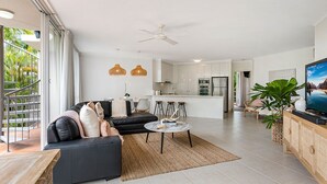 Ein modernes Wohnzimmer mit einer schwarzen Couch, einem Couchtisch und einem Fernseher auf einer Holzkommode.
