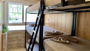 Une chambre avec un lit superposé, une fenêtre, des murs en bois et une étagère contenant des articles de toilette.
