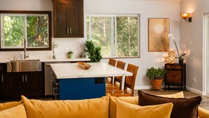 Una cocina moderna con una isla central, armarios oscuros y un comedor con sillas de madera.