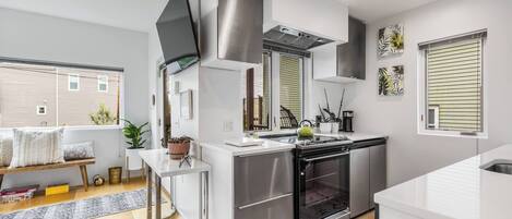 A modern kitchen with stainless steel appliances, a built-in oven, and a window with blinds.