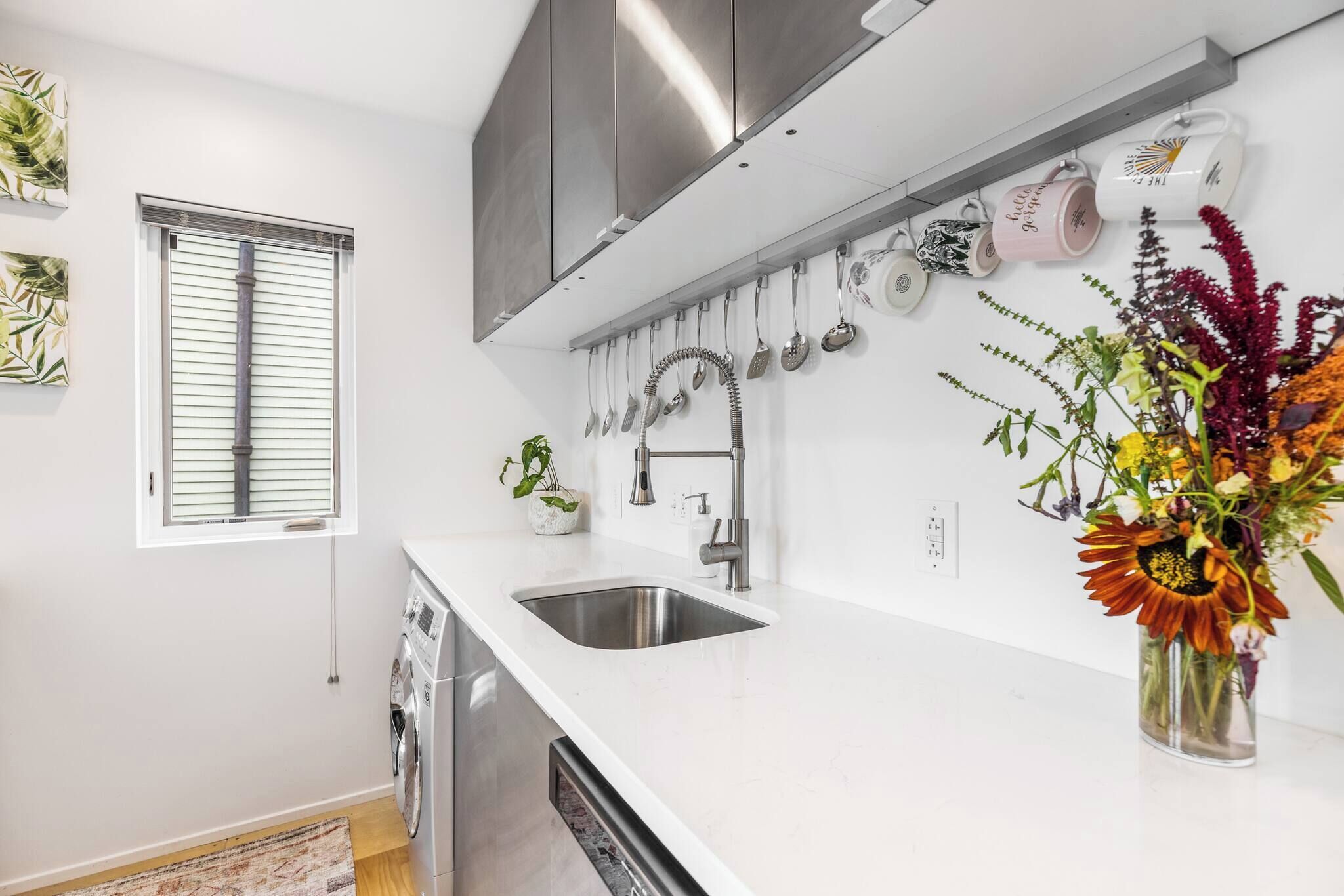 A modern kitchen with a stainless steel sink, a built-in dishwasher, and a hanging utensil rack.