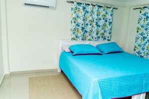 Een slaapkamer met een bed, bloemen gordijnen en een witte airconditioning aan de muur.