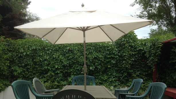 Eine Terrassenanlage mit Tisch und vier Stühlen, einem Sonnenschirm und einer Hecke im Hintergrund.
