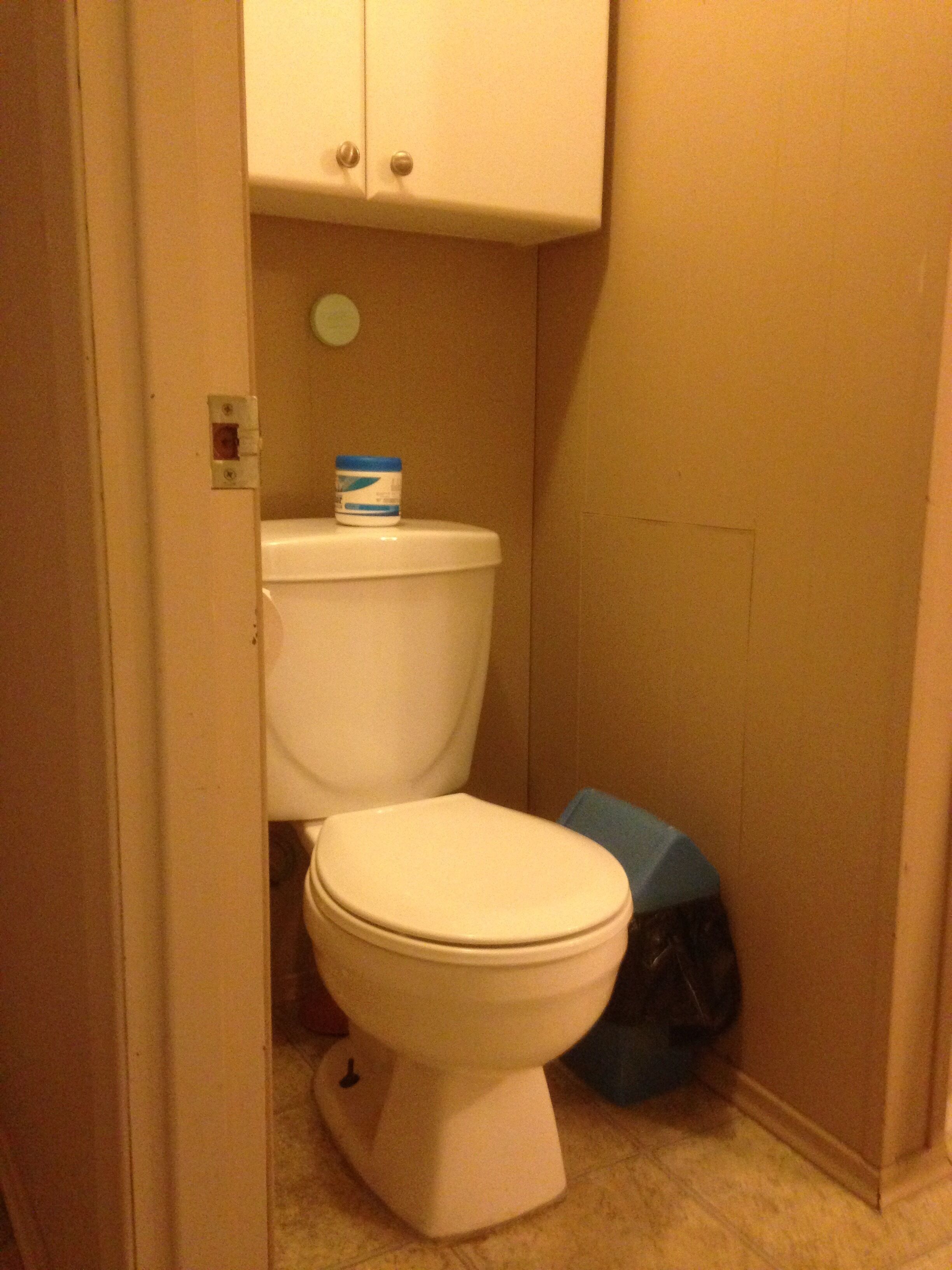 Un baño pequeño y funcional con inodoro, un armario encima y un cubo de basura azul al lado del inodoro.