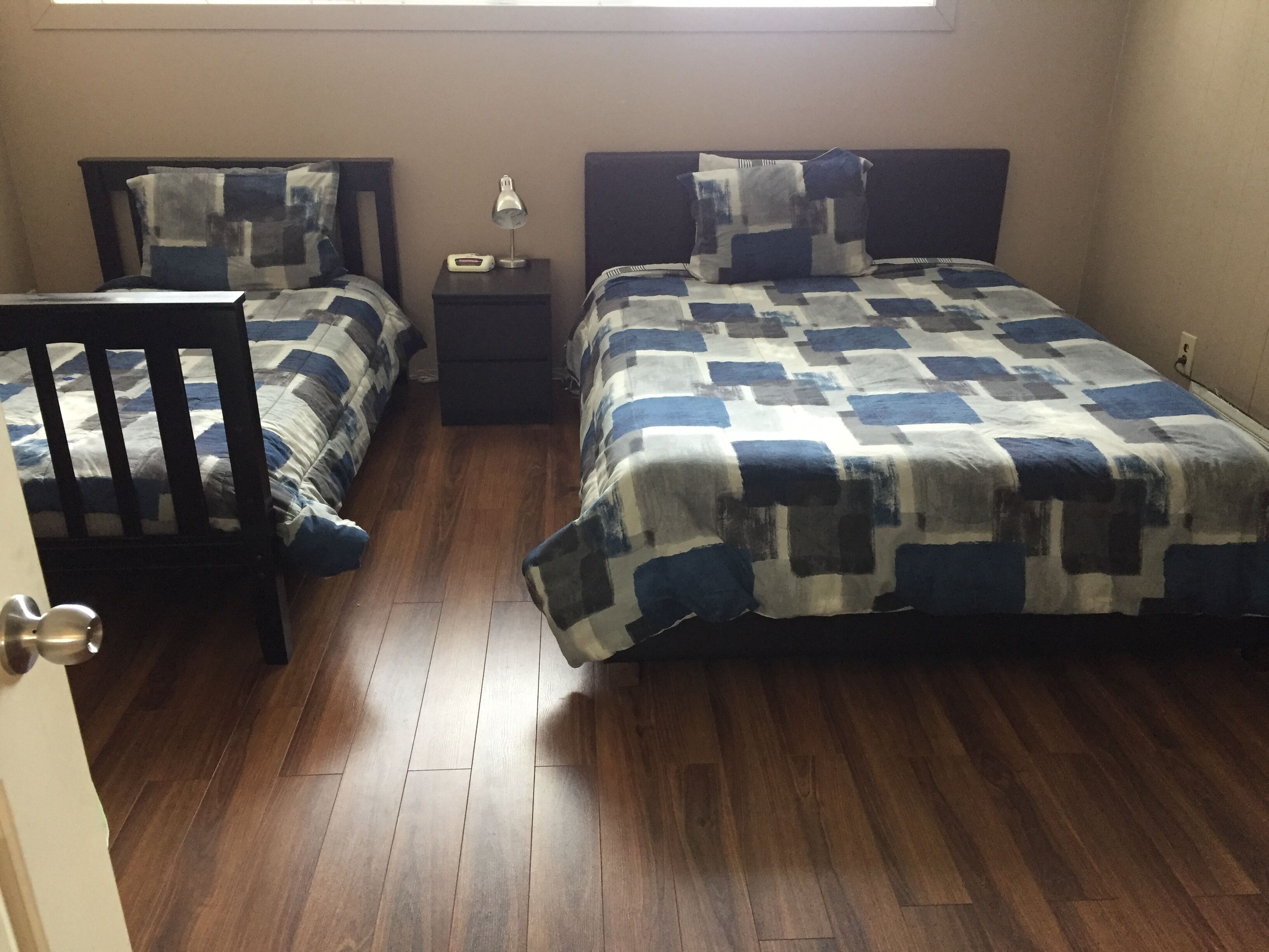 A bedroom with two beds, a nightstand, a chair, and a window.