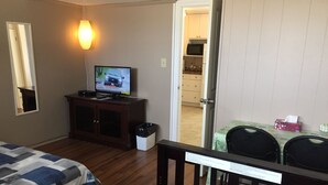 Ein Hotelzimmer mit Bett, Schreibtisch mit Computer, Fernseher und Blick auf die Küche durch eine offene Tür.