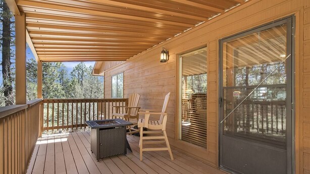 Una terraza de madera con pérgola, mobiliario exterior y una chimenea.
