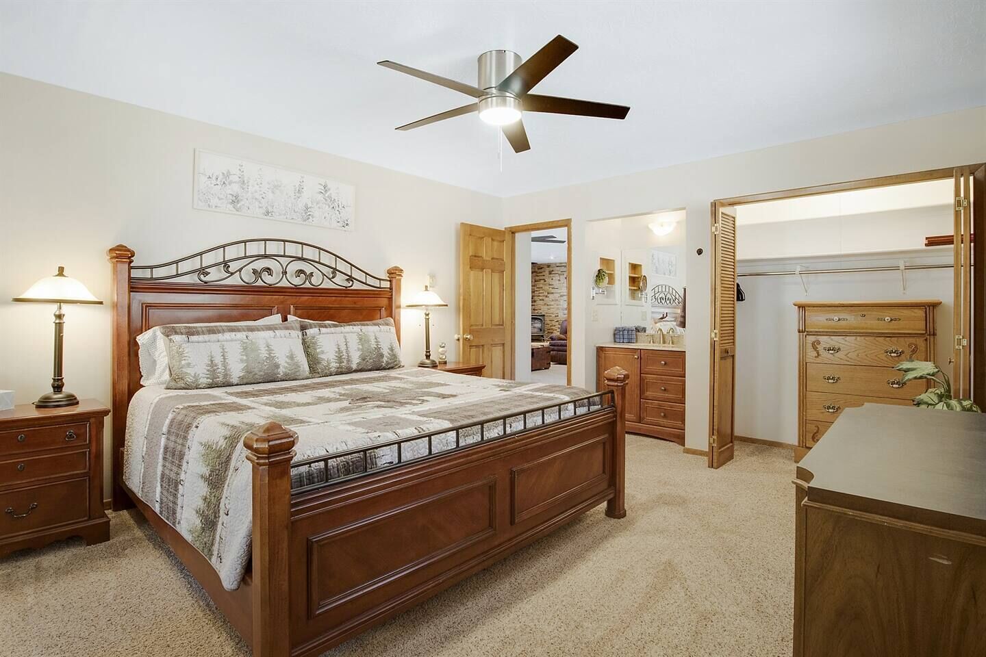 Ein Schlafzimmer mit einem hölzernen Bett, Nachttischlampen, einem Deckenventilator, einem Holzschrank und einem begehbaren Kleiderschrank.