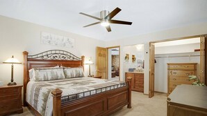 Un dormitorio con una cama de madera, lámparas de noche, ventilador de techo, cómoda de madera y vestidor.