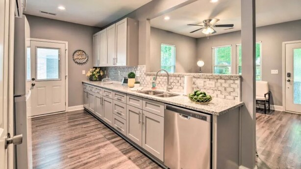 A modern kitchen with grey cabinets, a stainless steel dishwasher, and a tiled backsplash. - NEW! Centrally Located Charlotte Home by Amtrak! (Charlotte)