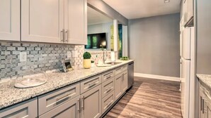 A modern kitchen with grey cabinets, a granite countertop, and a wooden floor. - NEW! Centrally Located Charlotte Home by Amtrak! (Charlotte)