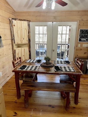 Comedor de madera con una mesa grande, bancos y vistas a través de puertas de vidrio.