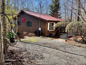 A wooden cabin with a red star decoration, a gravel driveway, and a wooden deck. - Creekfront Cabin with Waterfall, Hot Tub, Fire Pit (Ellijay)