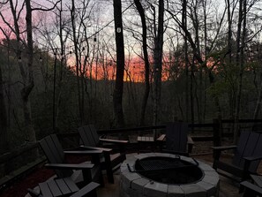 Un espacio al aire libre con sillas y una chimenea, rodeado de árboles.