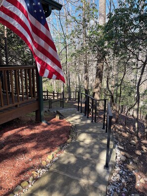 A wooden pathway with a metal railing, surrounded by trees and a large American flag. - Creekfront Cabin with Waterfall, Hot Tub, Fire Pit (Ellijay)