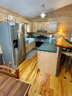 Une cuisine compacte avec des meubles en bois, un réfrigérateur en acier inoxydable, une cuisinière encastrée et un îlot central en bois doté de tabourets de bar.