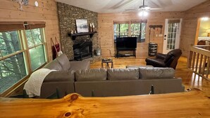Un accogliente interno di una baita con un camino in pietra, un ampio divano componibile e un patio in legno.