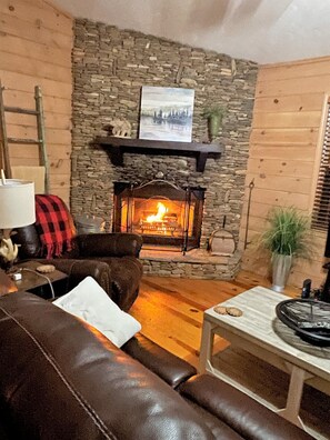 A cozy living room with a stone fireplace, a leather sofa, a wooden coffee table, and a lamp.