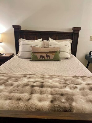 A bed with a textured blanket, a wooden headboard, and decorative pillows. - Creekfront Cabin with Waterfall, Hot Tub, Fire Pit (Ellijay)