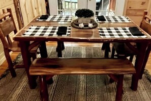 A wooden dining table with checkered placemats, a central potted plant, and a bench.