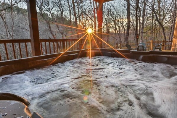 A hot tub with a wooden deck and a view of trees in the background.