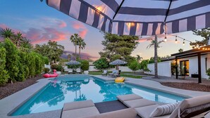A swimming pool with lounge chairs and umbrellas, surrounded by trees and a sunset view. - Spacious Modern Oasis with Pool, Hot Tub, and Putting in Scottsdale (Phoenix)