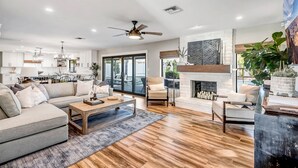 A spacious living room with a fireplace, a sofa, a coffee table, and a dining area visible through a glass door. - Spacious Modern Oasis with Pool, Hot Tub, and Putting in Scottsdale (Phoenix)
